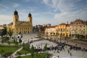 A debreceni Kossuth tér látképe a Református Nagytemplommal, környező történelmi épületekkel és szabadtéri rendezvénnyel, kora nyári napsütésben. Debrecen és Szeged környékén a legnagyobb a lakásdrágulás tempója.