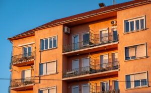 Narancssárga társasház erkélyekkel és ablakokkal, napsütésben.