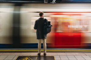 Férfi hátizsákkal vár a peronon, miközben elsuhan mellette egy piros-fehér metró szerelvény.
