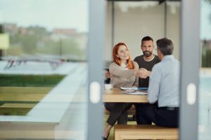 Ingatlanközvetítő (háttal) kezet ráz az ügyfeleivel a sikeres megbízási tárgyalás után. 