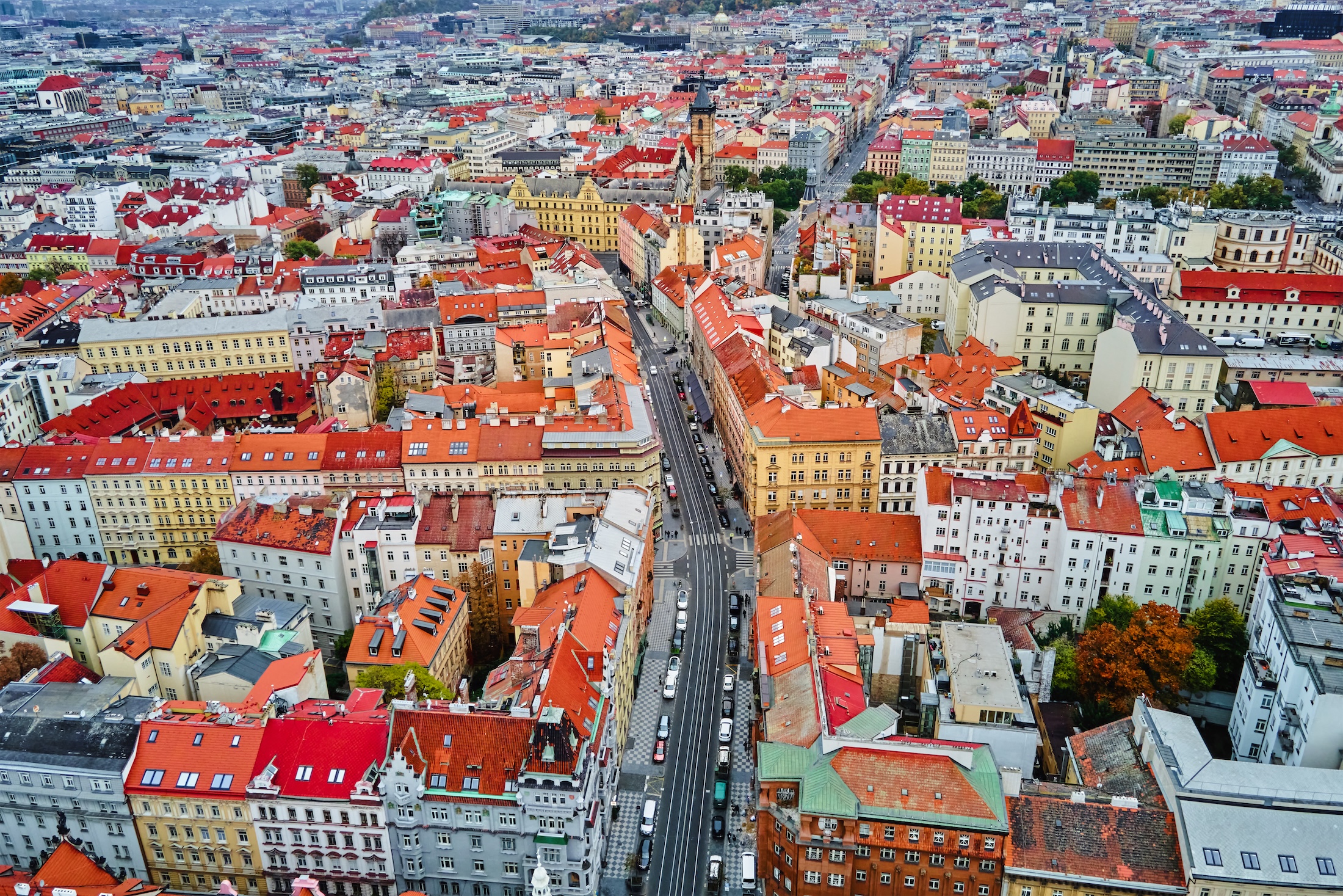 Légi felvétel egy sűrűn beépített történelmi belvárosról, ahol szorosan egymás mellett álló, többemeletes házak és vörös cseréptetők uralják a látképet. A városszövetet egy hosszú, egyenes út szeli ketté, az út mentén autók sorakoznak és haladnak. A kép sokszínű homlokzatú, klasszikus európai városi épületeket mutat, a háttérben templomtornyokkal és nagyobb középületekkel. A felvétel a város sűrű, történelmi jellegét és egységes tetővilágát hangsúlyozza.